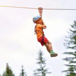 Happy kid with helmet and harness on zip line between trees