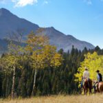 Three people horseback riding through mountains
